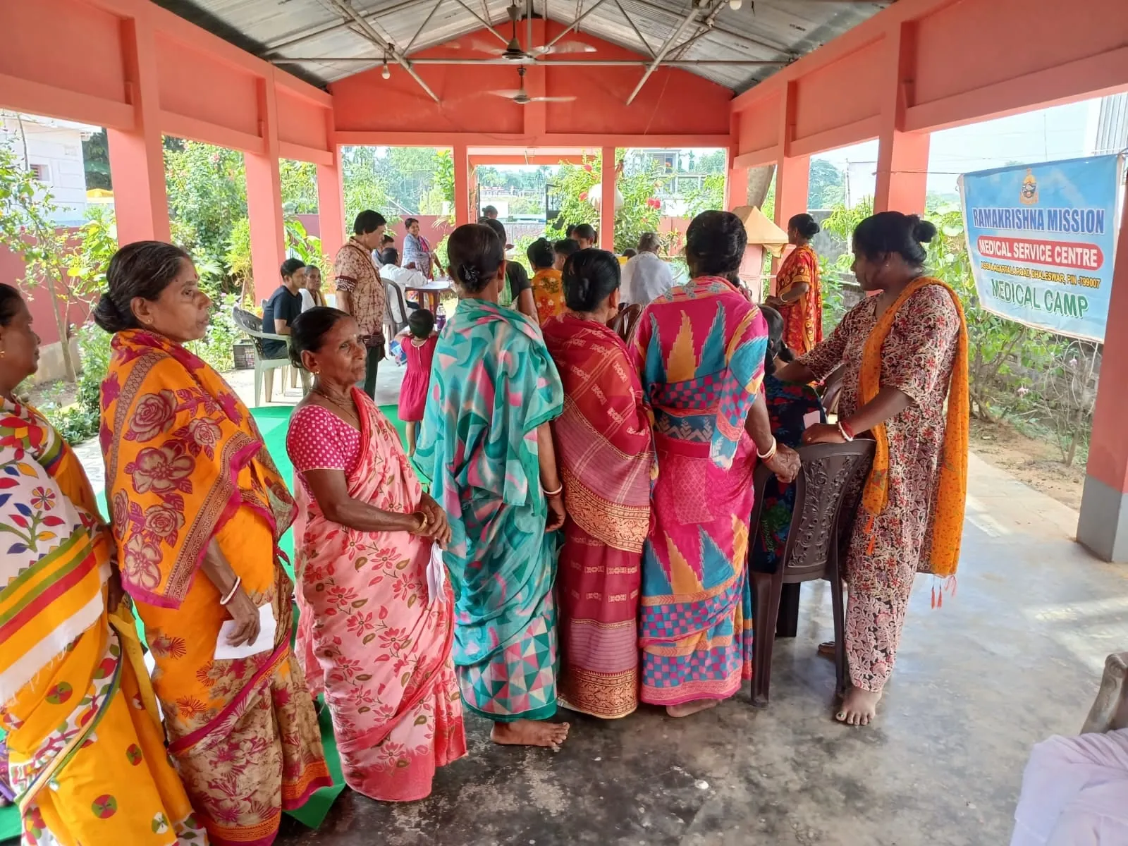 Women waiting at a mobile medical camp run by the Mission, beneath a Medical Service Centre banner